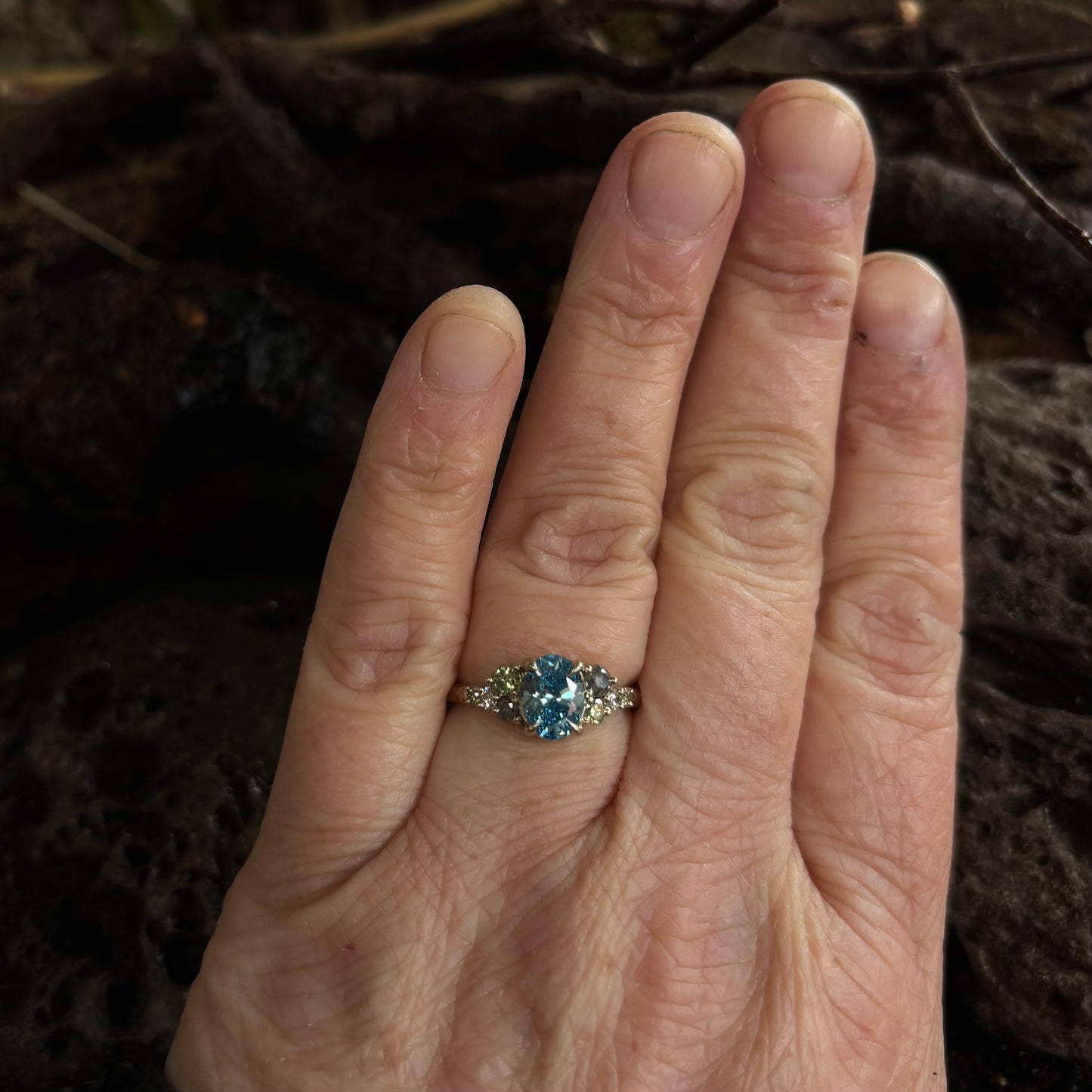 Hand wearing a ring with a blue gemstone against a dark background