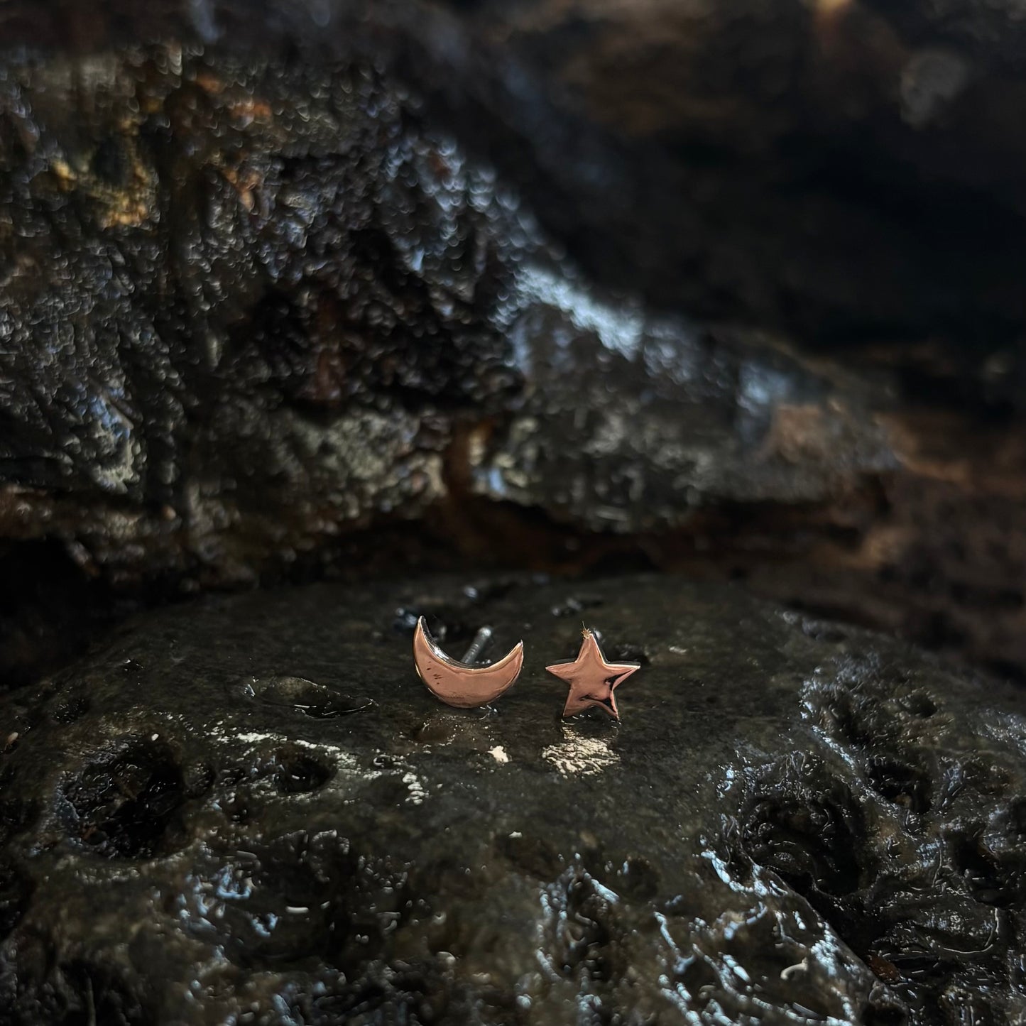 Rose gold moon and star earrings on a dark textured surface