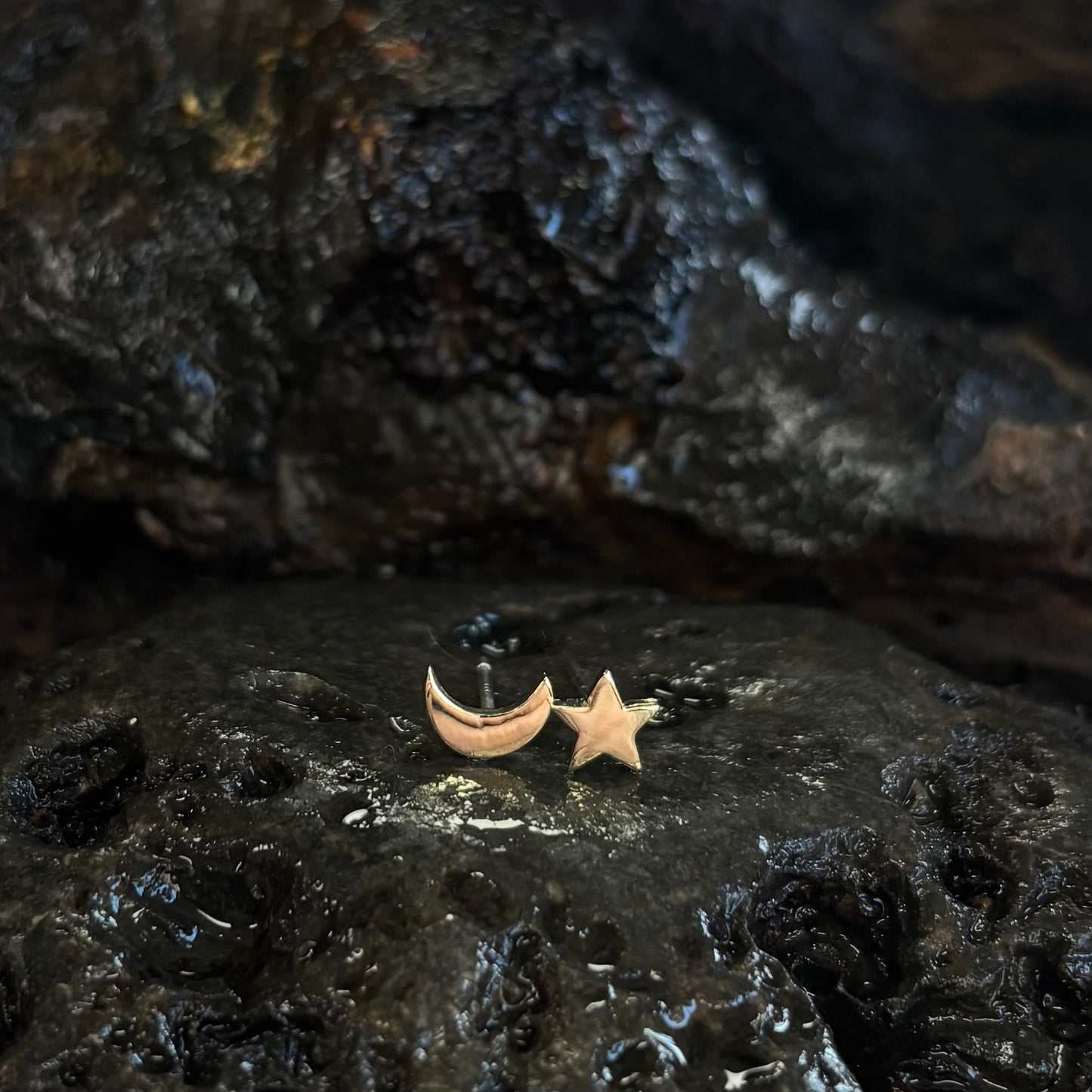 Gold star and crescent moon earrings on a dark stone surface