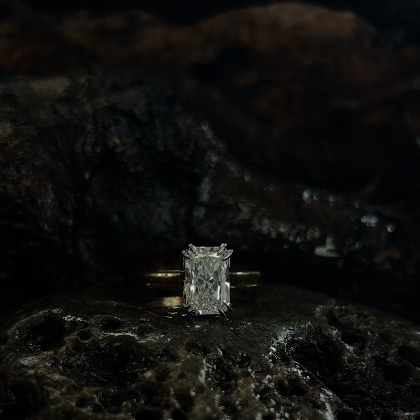 A radiant cut lab grown diamond solitaire ring with a platinum double claw talon mount and an 18ct yellow gold band, displayed on a dark textured surface.