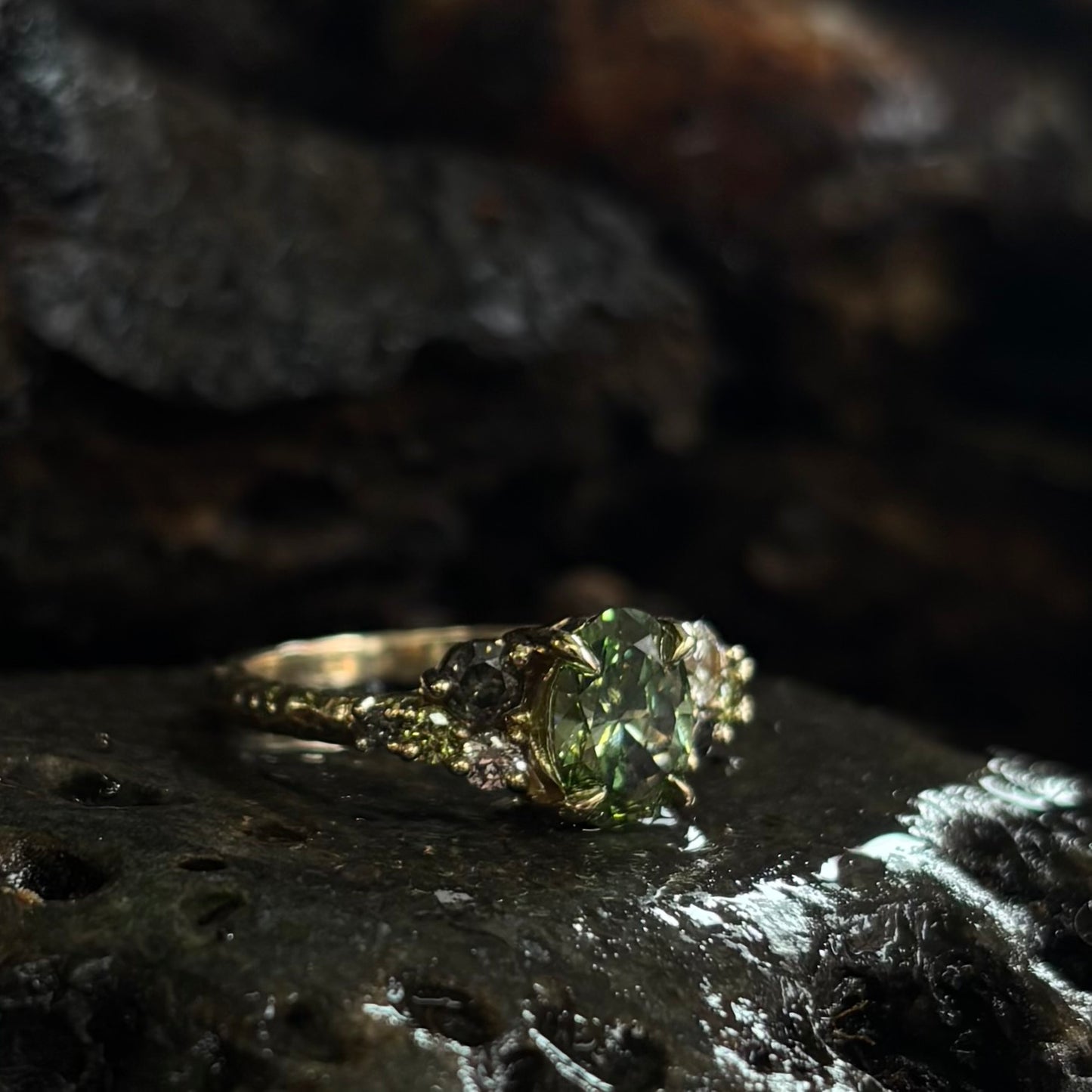 3/4 view Ring with a Central green gemstone and grey green and white accent stones on a dark textured surface
