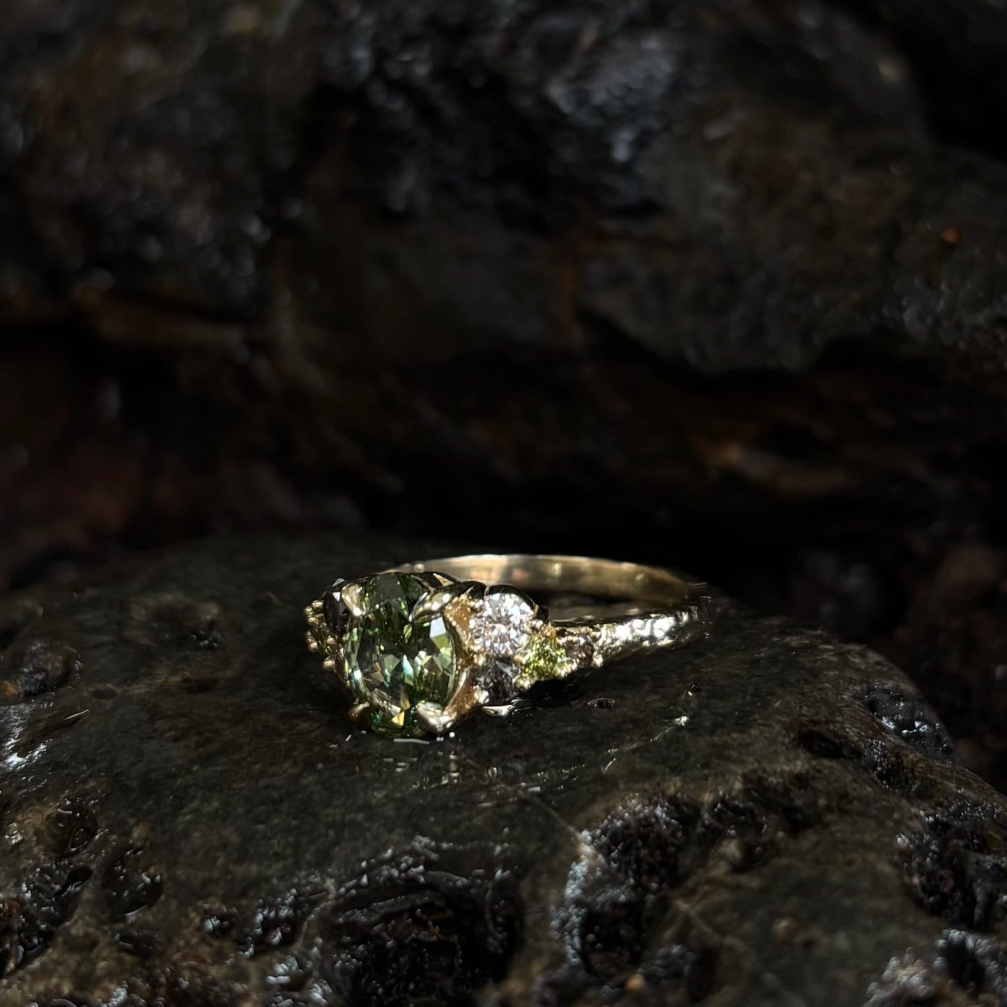 Ring with a Central green gemstone and grey green and white accent stones on a dark textured surface