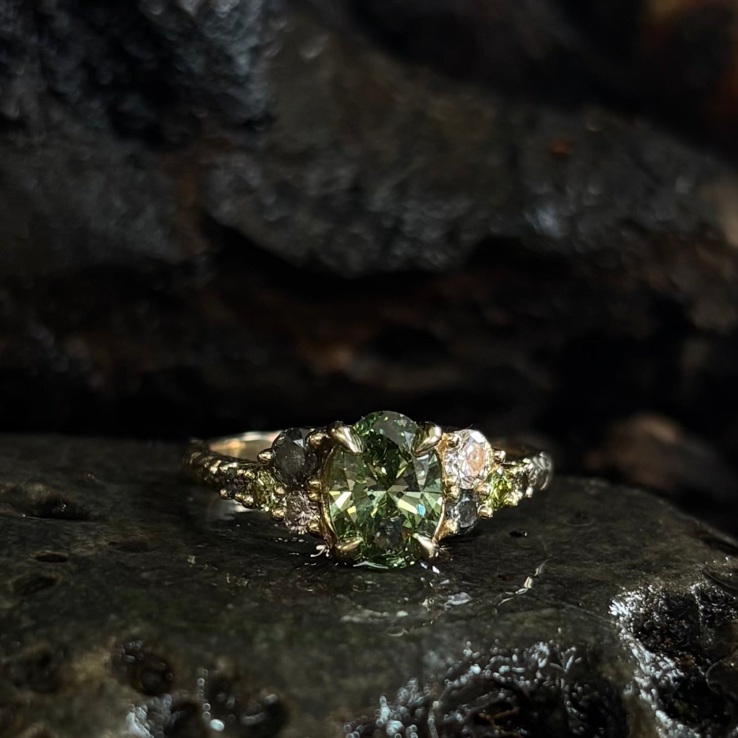Ring with a Central green gemstone and grey green and white accent stones on a dark textured surface