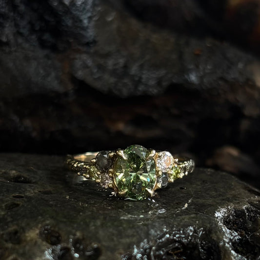 Ring with a Central green gemstone and grey green and white accent stones on a dark textured surface