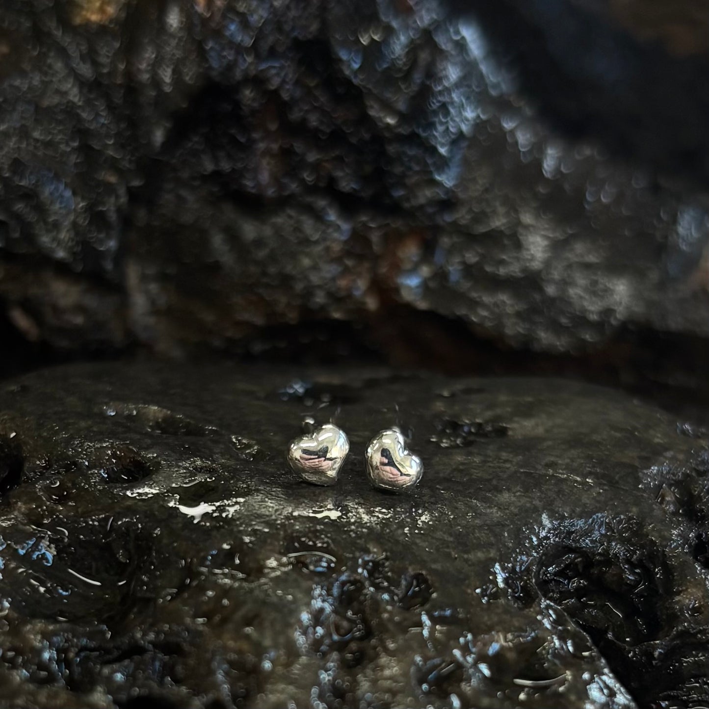 Pair of silver heart-shaped earrings on a dark, textured surface