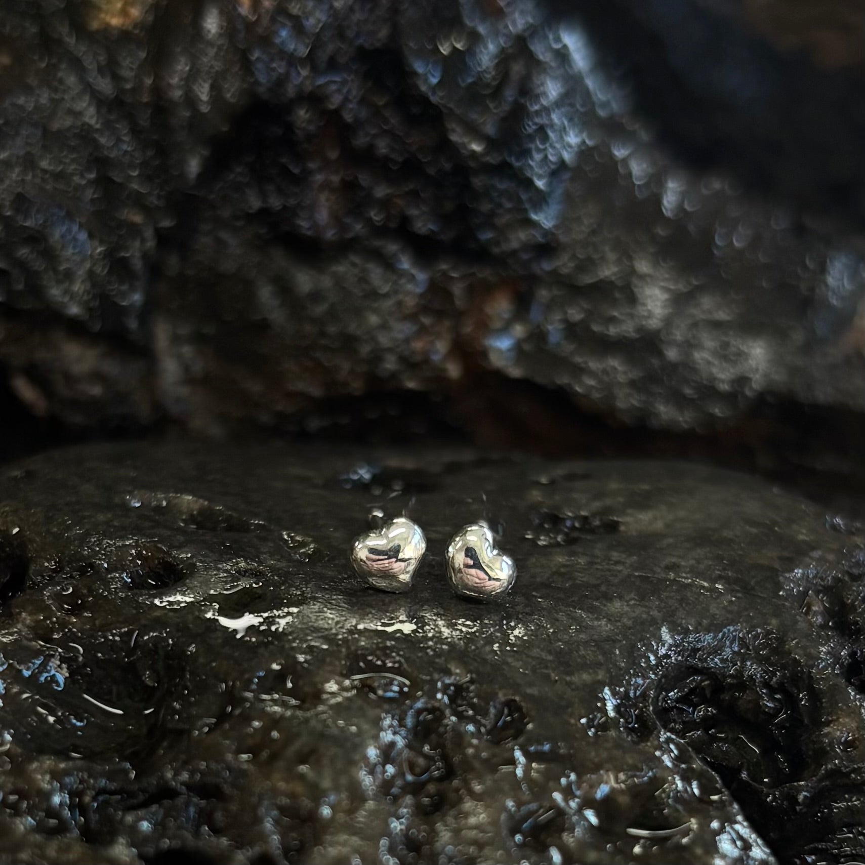 Pair of silver heart-shaped earrings on a dark, textured surface