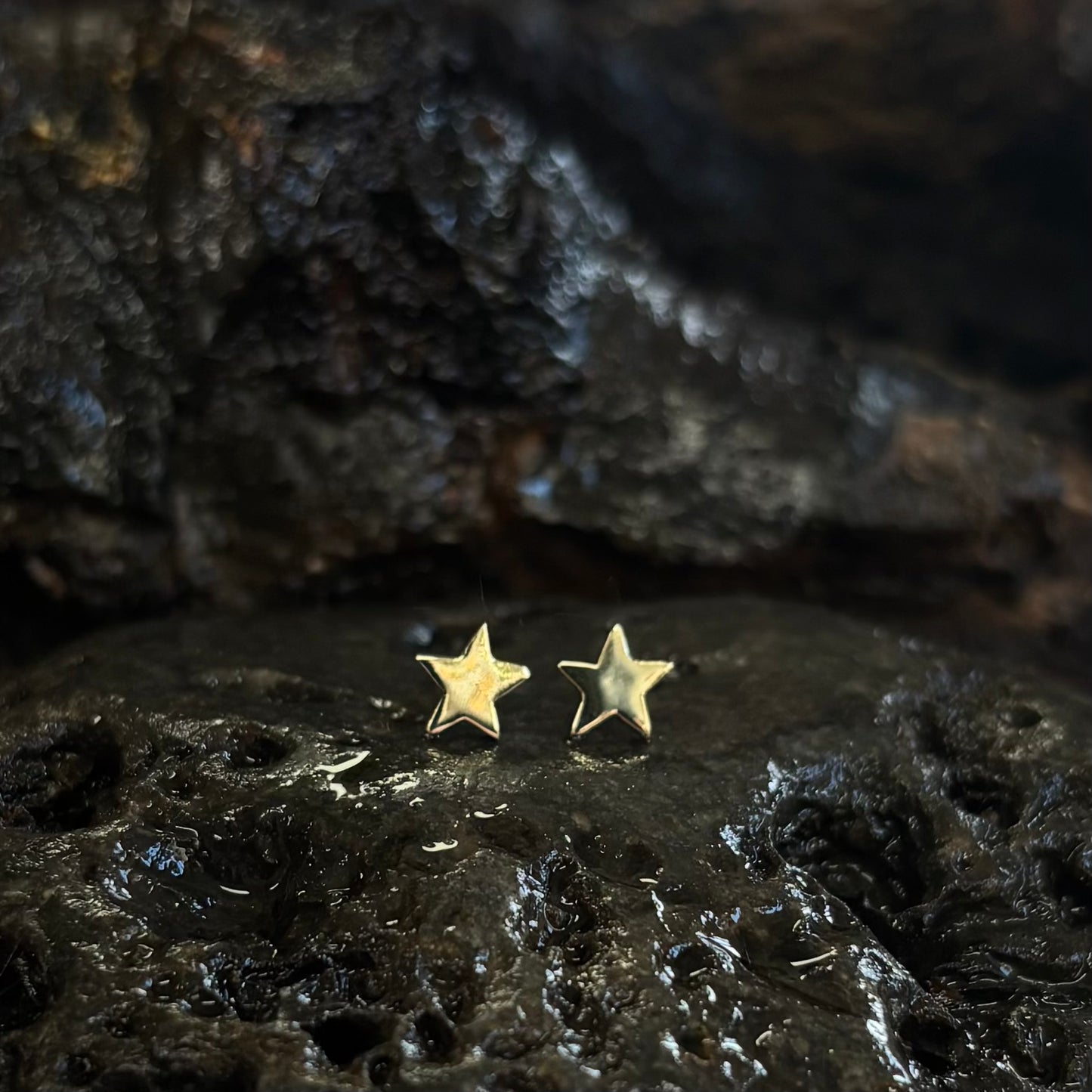 Gold star-shaped earrings on a dark, textured surface