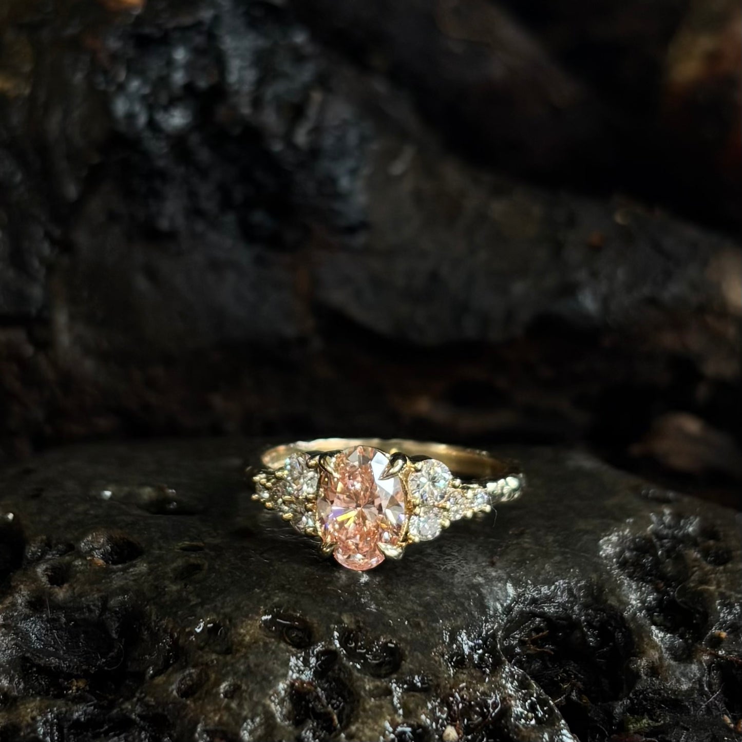  3/4 view Yellow gold Diamond ring with a pink gemstone on dark textured stone surface