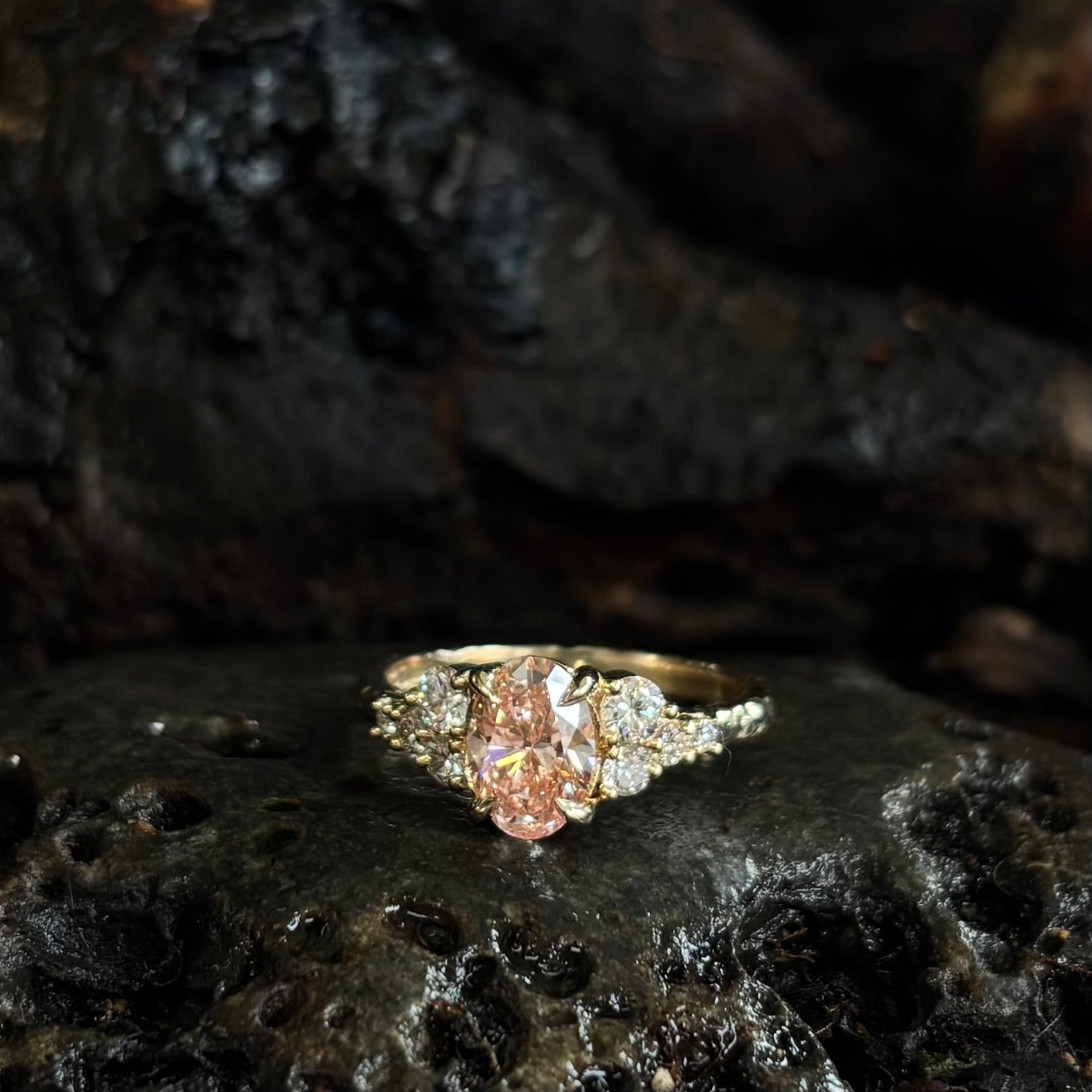  3/4 view Yellow gold Diamond ring with a pink gemstone on dark textured stone surface