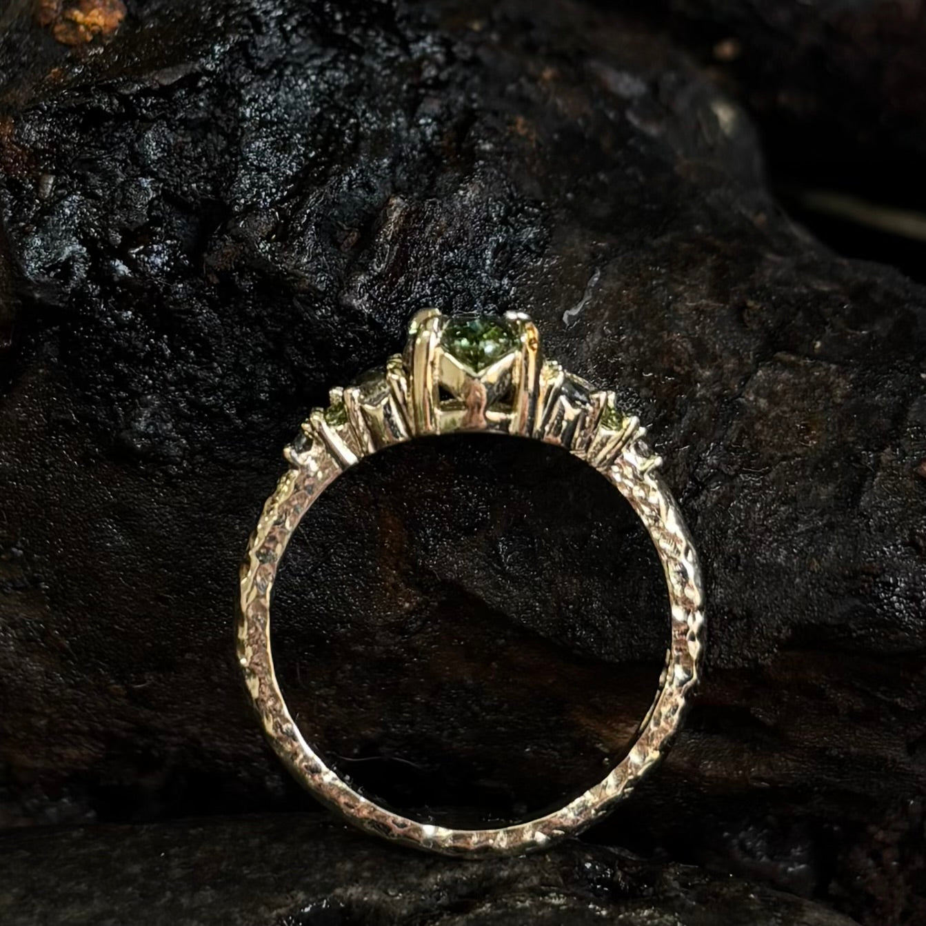 Side view Ring with a Central green gemstone and grey green and white accent stones on a dark textured surface