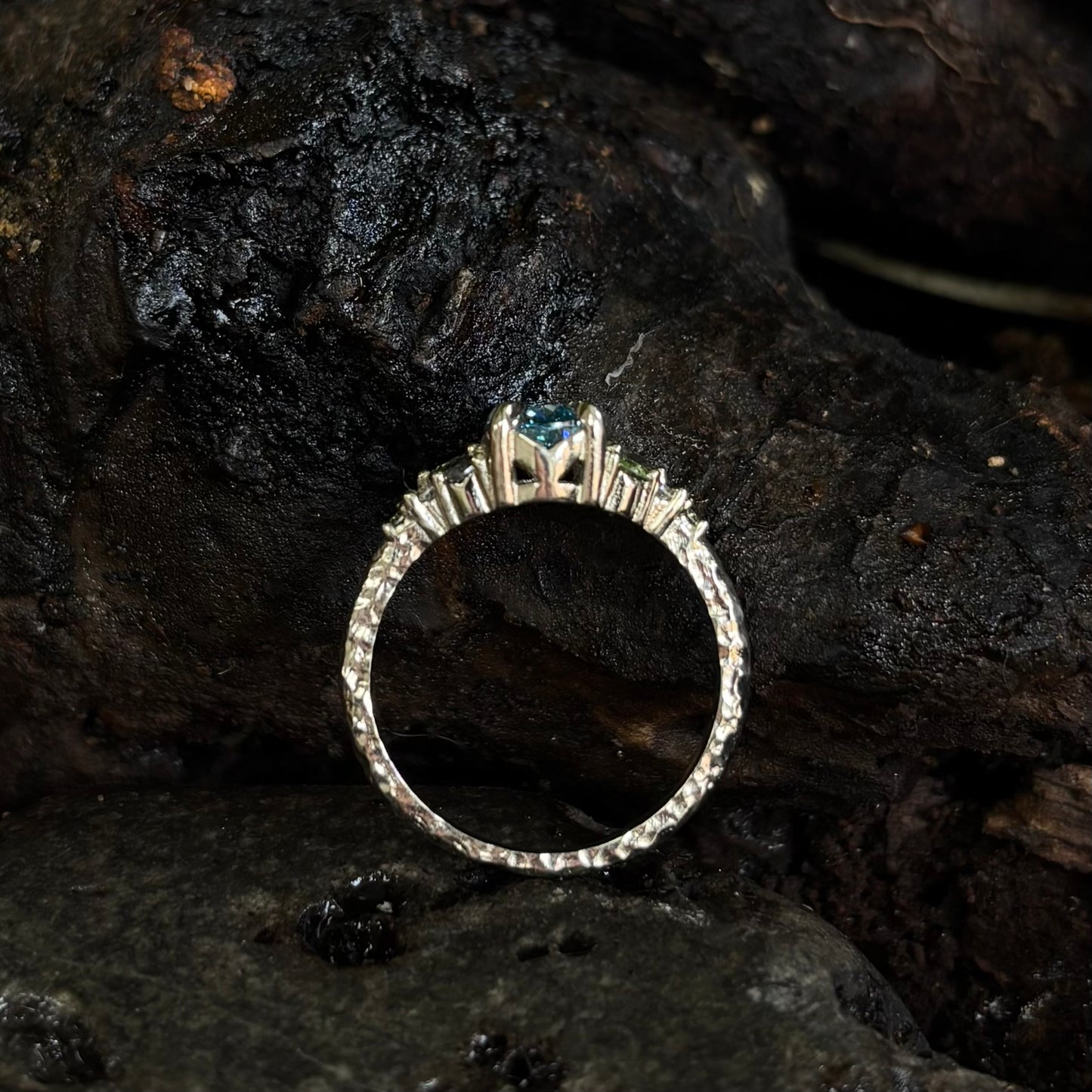 White gold ring with a central gemstone on a dark, textured surface