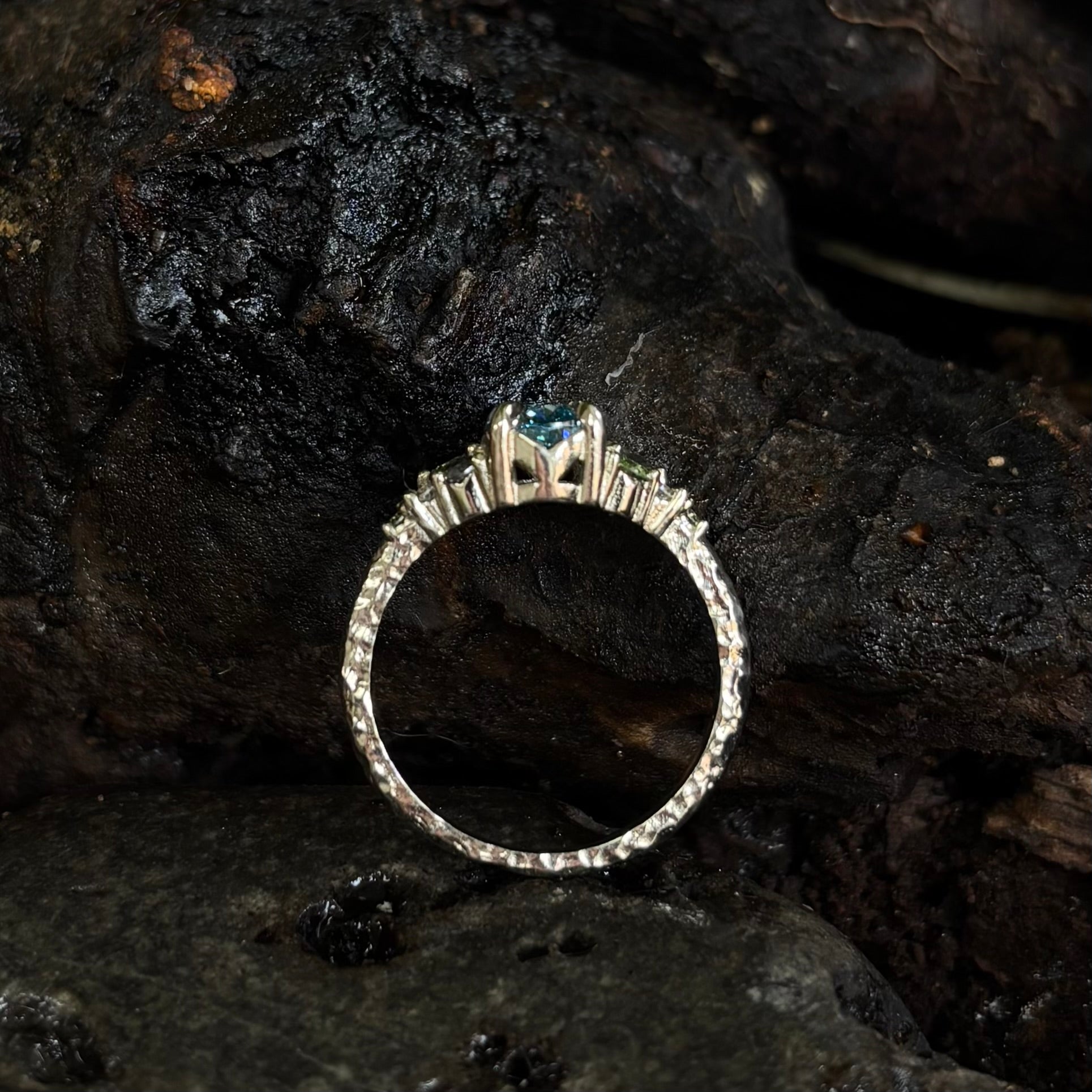 White gold ring with a central gemstone on a dark, textured surface