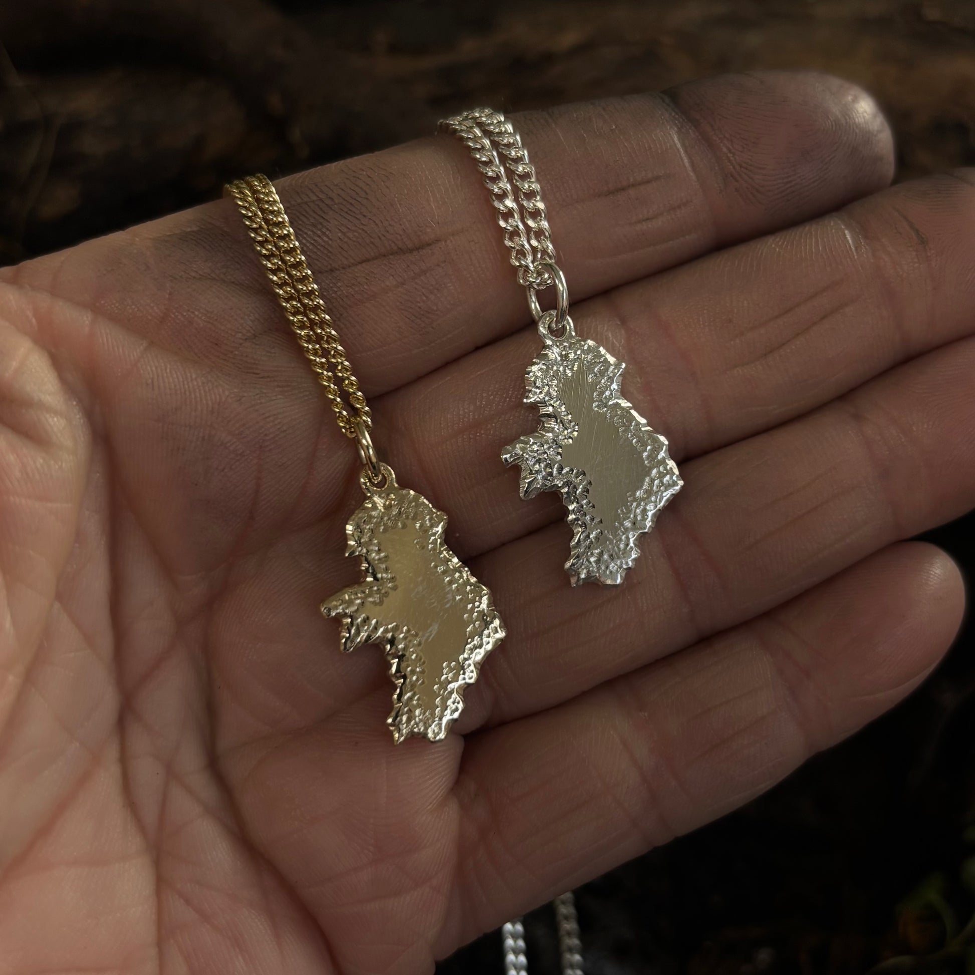 Two necklaces with map-shaped pendants on a hand.